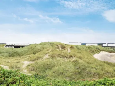 a grassy hill with a train in the background at 6 person holiday home in Brovst in Brovst