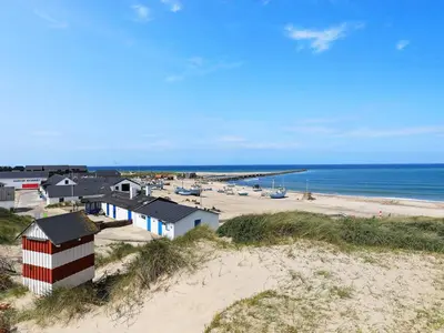 a beach with a red and white building and the ocean at 10 person holiday home in Thisted in Thisted