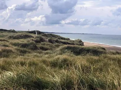 a beach with grass and the ocean on a cloudy day at 10 person holiday home in Thisted in Thisted