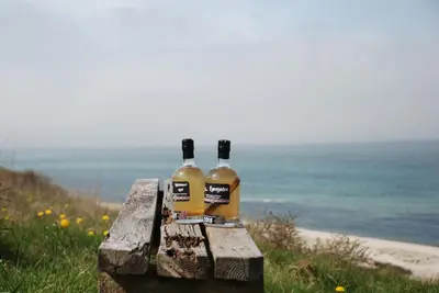 two bottles of wine sitting on a bench near the ocean at Sommerhus Farmen i Hanstholm in Hanstholm