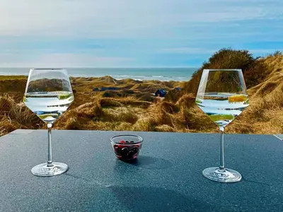 two glasses of wine sitting on a table near the beach at 6 person holiday home in Løkken in Løkken