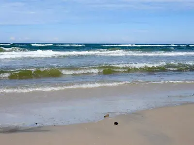 a beach with waves in the ocean on a sunny day at 6 person holiday home in Brovst in Brovst