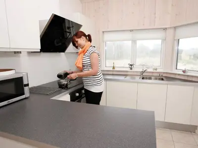 a woman standing in a kitchen cooking in a pot at Luxury Beach House in Blokhus - By Traum Ferienwohnungen in Blokhus