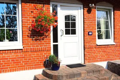 a red brick house with a white door and flowers at Fewo Skjærnsøde in Fjerritslev