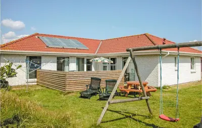 a house with a swing and a house with a solar roof at Nice Home In Blokhus With Sauna in Blokhus