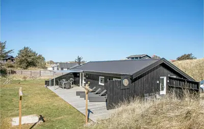 a black building with a deck in a field at Holiday Home Tobaksvej in Blokhus