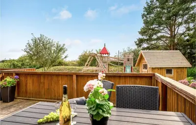 a table with a bottle of wine and flowers on a deck at Lovely Home In Thyholm With Sauna in Thyholm