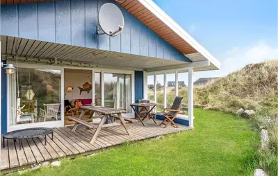 a blue house with a deck with a table and chairs at Holiday Home Svenstibakkevej Denm in Frøstrup