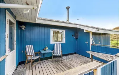 a blue house with two chairs and a table on a deck at Holiday Home Svenstibakkevej Denm in Frøstrup