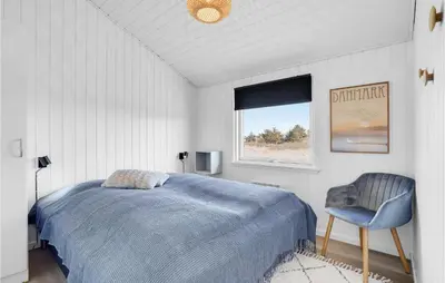 a bedroom with a bed and a chair and a window at Holiday Home Hermodsvej Harboøre Xi in Harboør