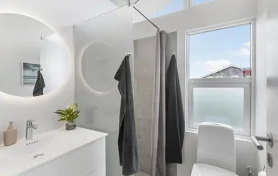 a white bathroom with a window and a sink at Holiday Home Monasvej Løkken Iv in Løkken