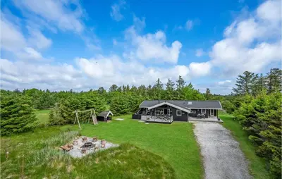 a black house with a playground in the grass at Holiday Home Jægerens Vej in Blokhus