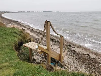 a wooden bench sitting on the side of a beach at 6 person holiday home in Lemvig-By Traum in Lemvig