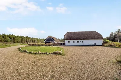 a white barn with a straw roof on a gravel field at Lildgaard in Frøstrup
