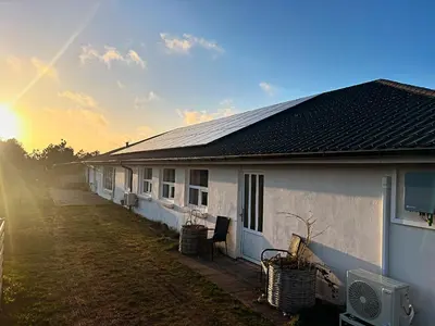 a white house with the sun setting behind it at Stone Mountain BnB in Stenbjerg