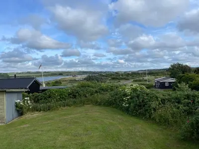 a view of a field with a house and a river at Ældre Sommerhus Max 4 voksne og 4 børn in Lemvig
