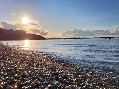 a rocky beach with the sun setting over the water at 10 person holiday home in Roslev-By Traum in Roslev