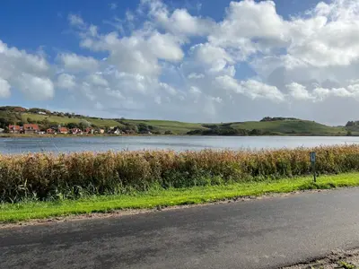 a road next to a large body of water at Hyggeligt byhus in Harboør