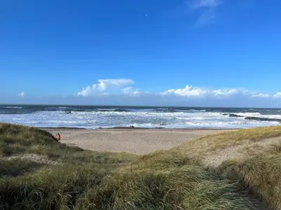 a beach with the ocean and a person sitting on the sand at Hyggeligt byhus in Harboør
