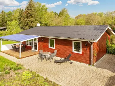 a small red house with a patio and a table at 6 person holiday home in Nibe-By Traum in Nibe
