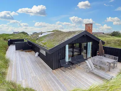 a black house with a wooden deck with a table at 6 person holiday home in Saltum-By Traum in Saltum
