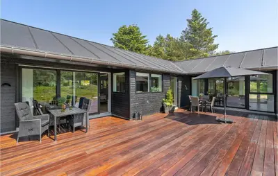 a house with a wooden deck with a table and an umbrella at 4 Bedroom Amazing Home In Blokhus in Blokhus