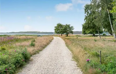 a gravel road through a field with trees and flowers at 3 Bedroom Cozy Home In Nibe in Nibe