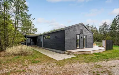 a black house in a field with trees at Amazing Home In Blokhus With Sauna in Blokhus