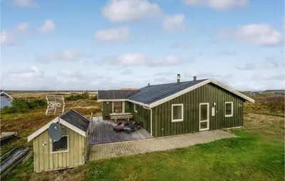 a green house with a deck in a field at Awesome Home In Lemvig With Wifi in Lemvig
