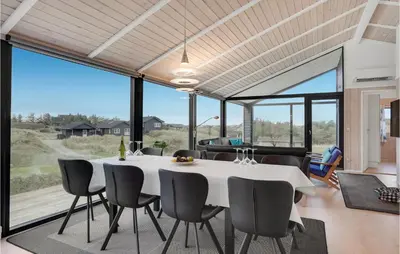 a dining room with a table and chairs and large windows at Cozy Home In Blokhus With Kitchen in Blokhus