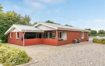 a red house with a patio in front of a lake at 2 Bedroom Awesome Home In Vemb in Vemb