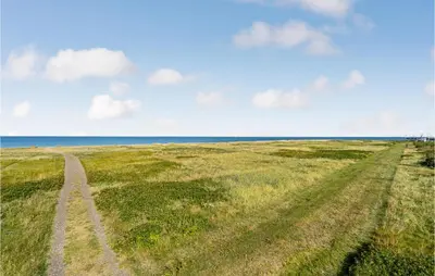 a field with tracks in the grass and the ocean at Lovely Home In Løgstør With Kitchen in Løgstør