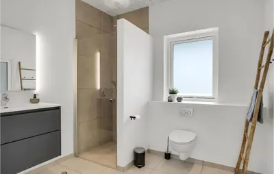 a bathroom with a toilet and a sink and a window at Nice Home In Blokhus With Sauna in Blokhus