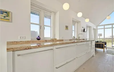 a kitchen with white cabinets and a sink and windows at Holiday Home Ved Stranden in Blokhus