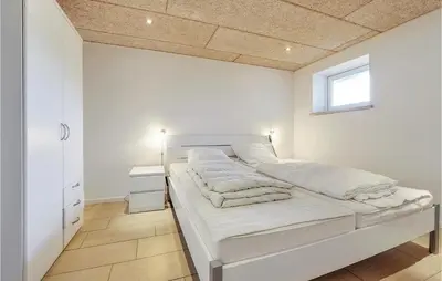 a bedroom with a bed with white sheets and a window at Holiday Home Ved Stranden in Blokhus
