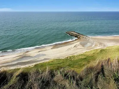 a rock sticking out of the sand next to the ocean at Holiday Home Ena - 75m from the sea by Interhome in Lemvig