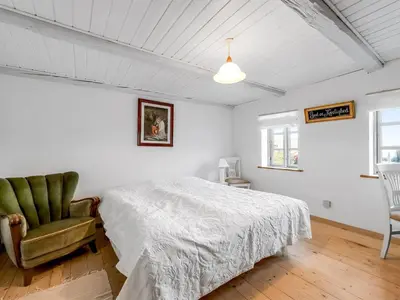a white bedroom with a bed and a chair at Holiday Home Orvo - 150m from the sea by Interhome in Harboør