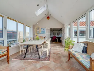 a living room with a table and chairs and windows at Holiday Home Pauli - 75m from the sea by Interhome in Harboør