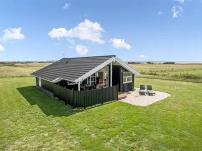 a small black house with two chairs in a field at Holiday Home Eemil - 700m from the sea by Interhome in Harboør