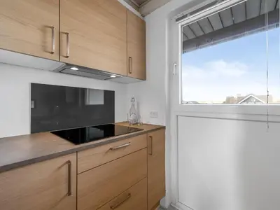 a kitchen with wooden cabinets and a large window at Holiday Home Iines - 200m from the sea by Interhome in Harboør