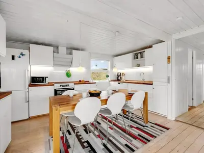 a kitchen with white cabinets and a wooden table and chairs at Holiday Home Amandus - 100m from the sea by Interhome in Harboør