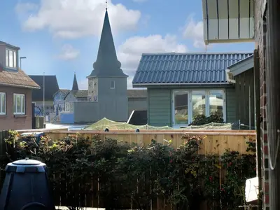 a church with a steeple in the background with a garden at Holiday Home Heming - 100m from the sea by Interhome in Thyborøn
