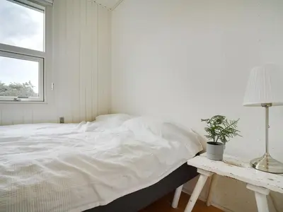 a white bedroom with a bed and a plant on a table at Holiday Home Vilja - 150m from the sea by Interhome in Torsted