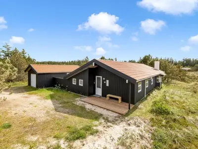 a black cottage with a wooden deck in a field at Holiday Home Antto - 900m from the sea by Interhome in Torsted