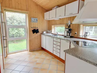 a kitchen with wooden walls and white cabinets and windows at Holiday Home Konrad - 400m from the sea by Interhome in Torsted