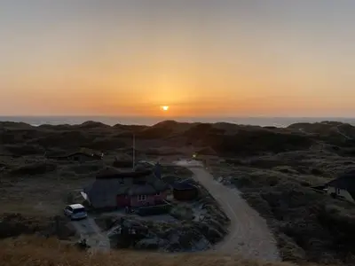 a sunset over a field with a house and the ocean at Holiday Home Tabea - 150m from the sea by Interhome in Løkken