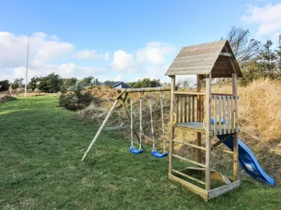 a playground with a swing set in a field at Holiday Home Vanamo - 300m from the sea by Interhome in Løkken
