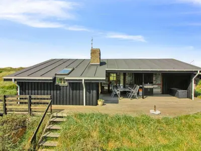 a black house with a deck and a table at Holiday Home Essie - 250m from the sea by Interhome in Løkken