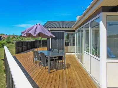 a wooden deck with a table and chairs and an umbrella at Holiday Home Dome - 750m from the sea by Interhome in Løkken