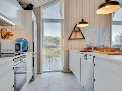 a kitchen with white cabinets and a large window at Holiday Home Marthine - 200m from the sea by Interhome in Løkken